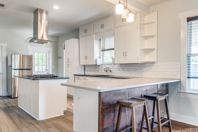 kitchen with tasteful backsplash, ventilation hood, decorative light fixtures, kitchen peninsula, and stainless steel appliances