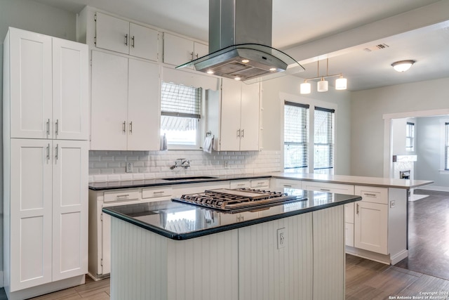 kitchen featuring island range hood, a kitchen island, a peninsula, white cabinetry, and a sink