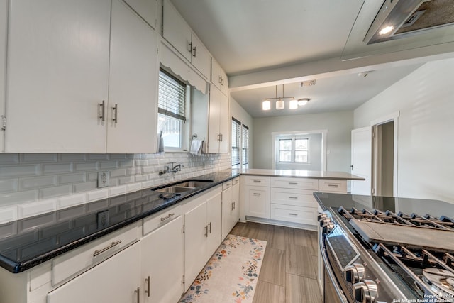 kitchen with a peninsula, a sink, white cabinetry, stainless steel range with gas cooktop, and dark countertops