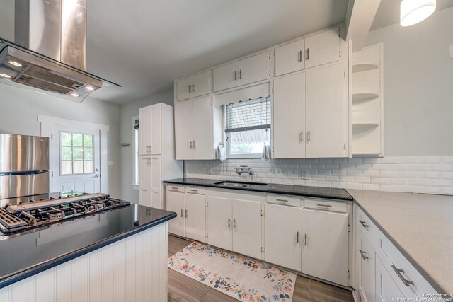 kitchen with appliances with stainless steel finishes, decorative backsplash, light hardwood / wood-style floors, range hood, and white cabinetry