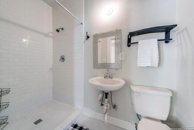 bathroom with tiled shower, sink, toilet, and tile patterned floors