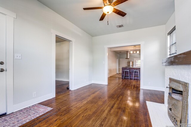 unfurnished living room featuring ceiling fan, dark wood-type flooring, and a fireplace