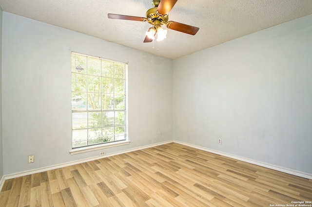 empty room with ceiling fan, light wood-type flooring, and a textured ceiling