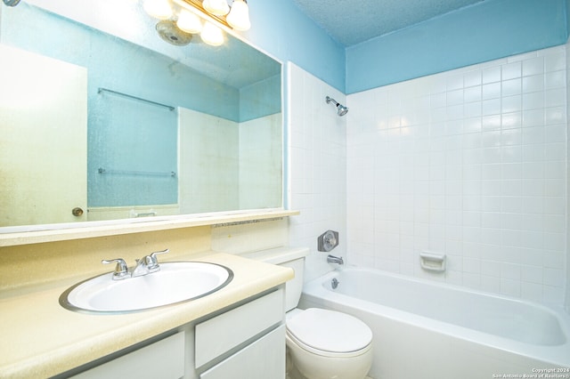 full bathroom featuring a textured ceiling, toilet, tiled shower / bath, and vanity