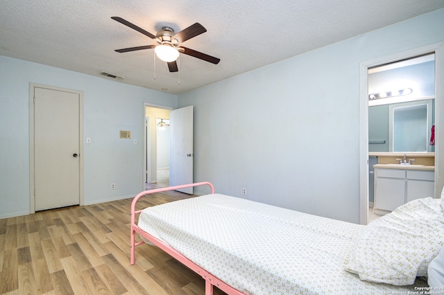 bedroom featuring sink, ensuite bath, light hardwood / wood-style flooring, a textured ceiling, and ceiling fan