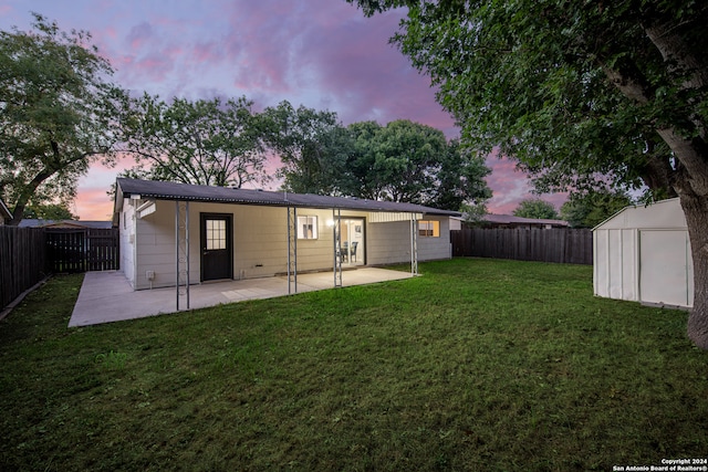 back house at dusk with a storage unit, a yard, and a patio area