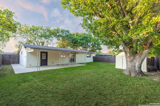 back house at dusk with a storage shed, a patio, and a yard