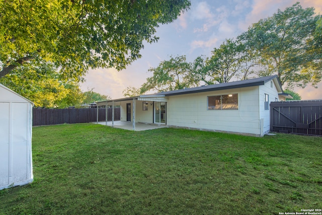 back house at dusk featuring a shed, a patio area, and a yard