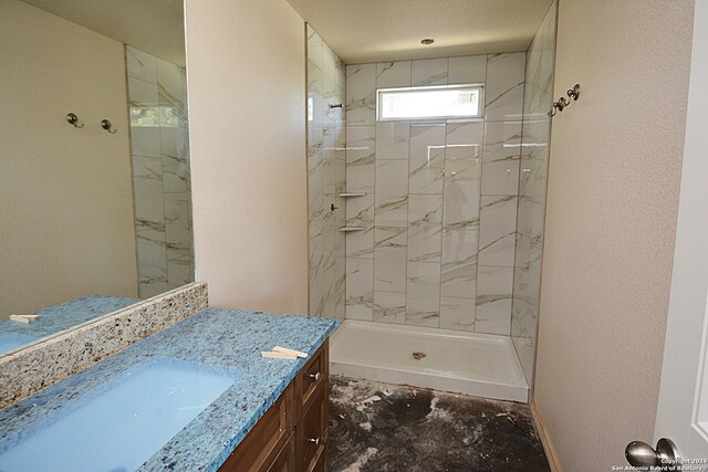 full bath featuring a textured wall, a tile shower, vanity, and baseboards