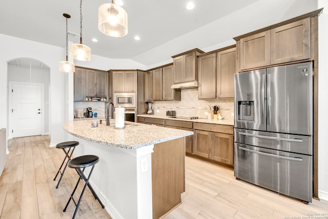 kitchen with backsplash, appliances with stainless steel finishes, light stone countertops, and light hardwood / wood-style floors