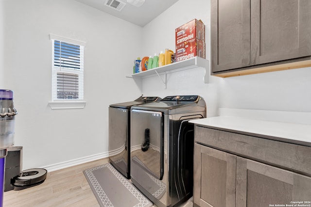 washroom featuring light wood-type flooring, washing machine and clothes dryer, and cabinets