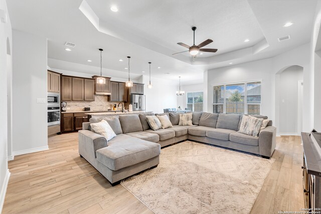 living room featuring ceiling fan, sink, a tray ceiling, and light hardwood / wood-style floors