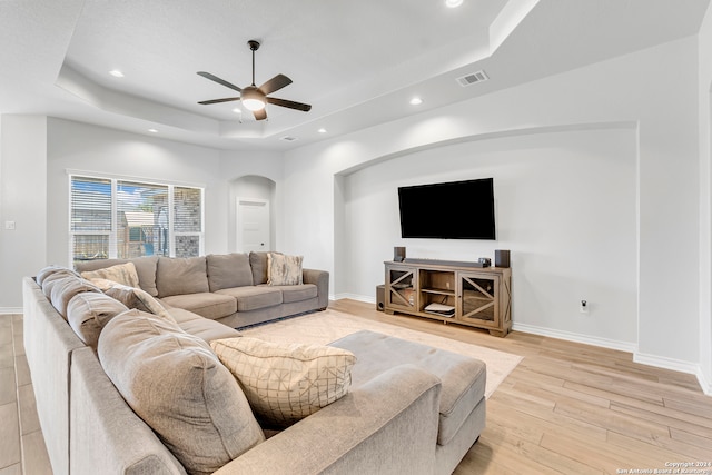 living room with a tray ceiling, light hardwood / wood-style flooring, and ceiling fan