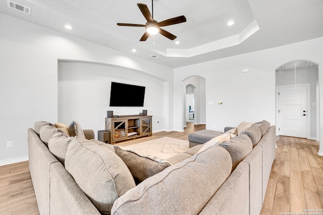 living room with ceiling fan, light hardwood / wood-style flooring, and a tray ceiling