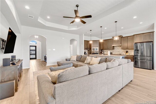 living room with light hardwood / wood-style flooring, ceiling fan, and a raised ceiling