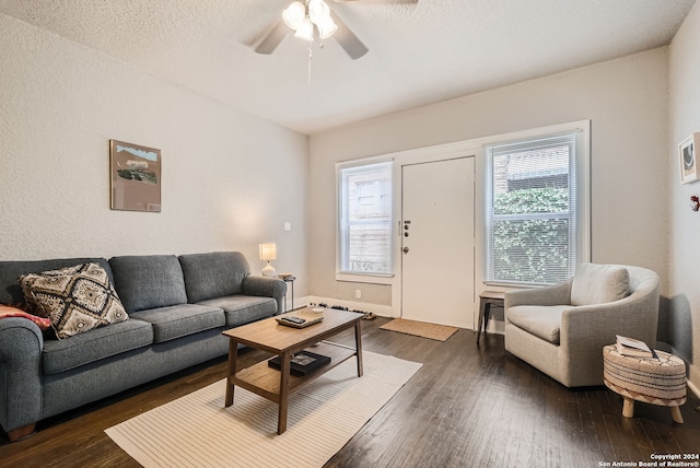 living room with ceiling fan, a textured ceiling, and dark wood-type flooring