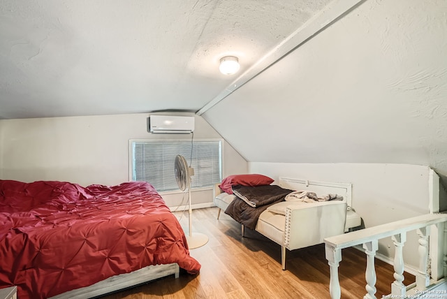 bedroom featuring light hardwood / wood-style flooring, a textured ceiling, a wall mounted AC, and lofted ceiling