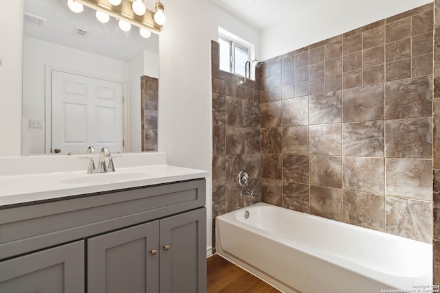 bathroom featuring hardwood / wood-style flooring, tiled shower / bath, a textured ceiling, and vanity