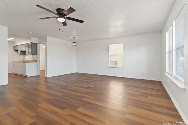 unfurnished living room featuring a wealth of natural light, a textured ceiling, dark wood-type flooring, and ceiling fan