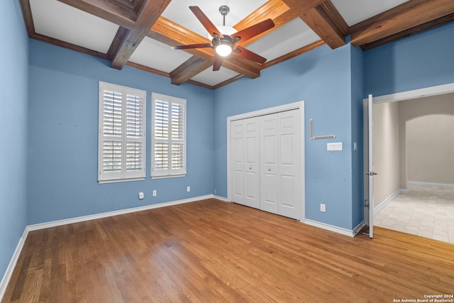 unfurnished bedroom featuring ceiling fan, beamed ceiling, coffered ceiling, a closet, and hardwood / wood-style floors