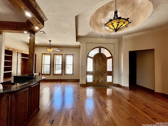 foyer entrance with hardwood / wood-style flooring, a textured ceiling, ceiling fan, a raised ceiling, and decorative columns