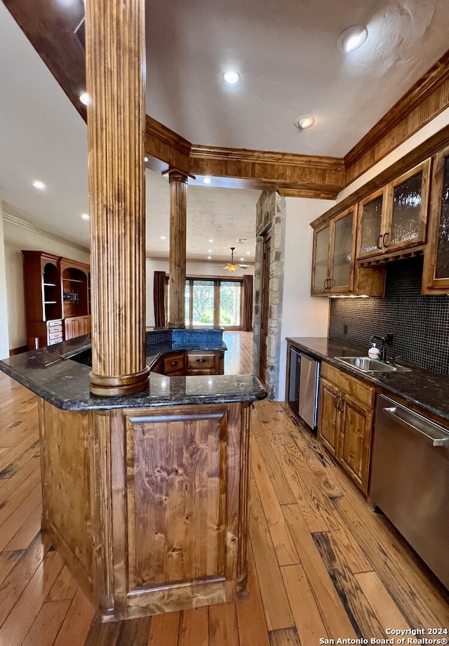 kitchen featuring dark stone counters, stainless steel dishwasher, light hardwood / wood-style flooring, decorative columns, and sink