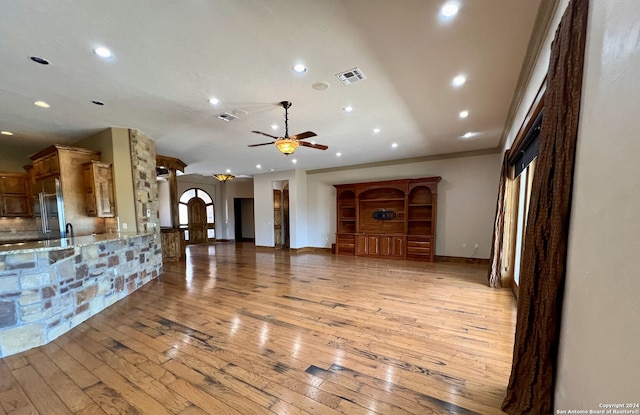 unfurnished living room featuring light hardwood / wood-style flooring, ceiling fan, and crown molding