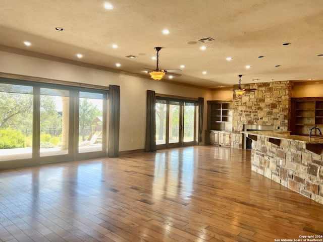 unfurnished living room featuring wood-type flooring, built in shelves, and a healthy amount of sunlight