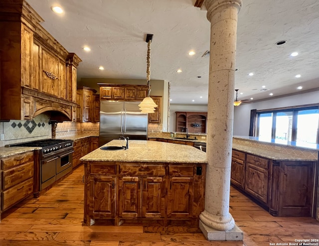 kitchen featuring ornate columns, light hardwood / wood-style flooring, high quality appliances, tasteful backsplash, and a center island with sink