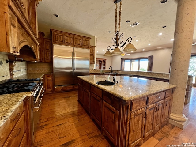 kitchen with decorative backsplash, sink, an island with sink, light wood-type flooring, and high end appliances