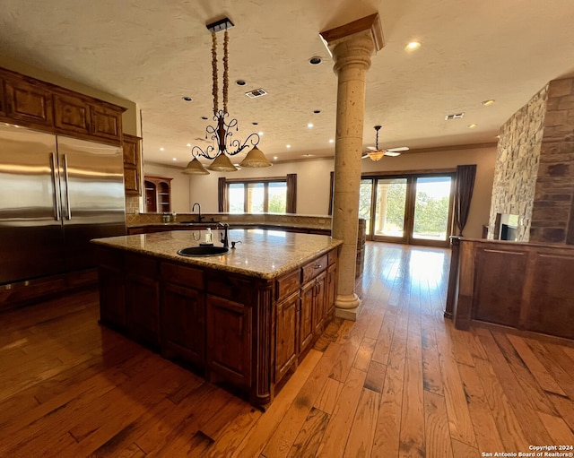 kitchen with a wealth of natural light, stainless steel built in refrigerator, light hardwood / wood-style floors, and an island with sink