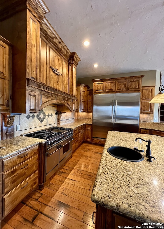 kitchen with backsplash, sink, light wood-type flooring, light stone countertops, and high quality fridge