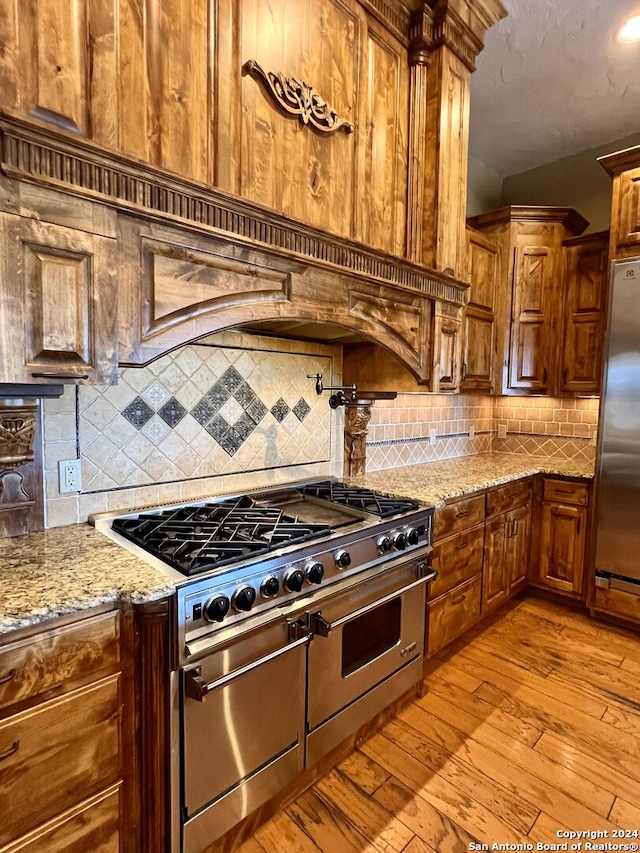 kitchen featuring light wood-type flooring, tasteful backsplash, light stone counters, and stainless steel appliances