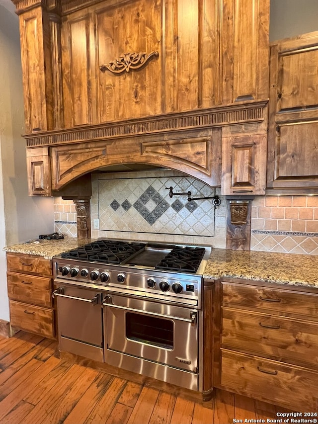 kitchen featuring hardwood / wood-style floors, backsplash, light stone counters, and double oven range