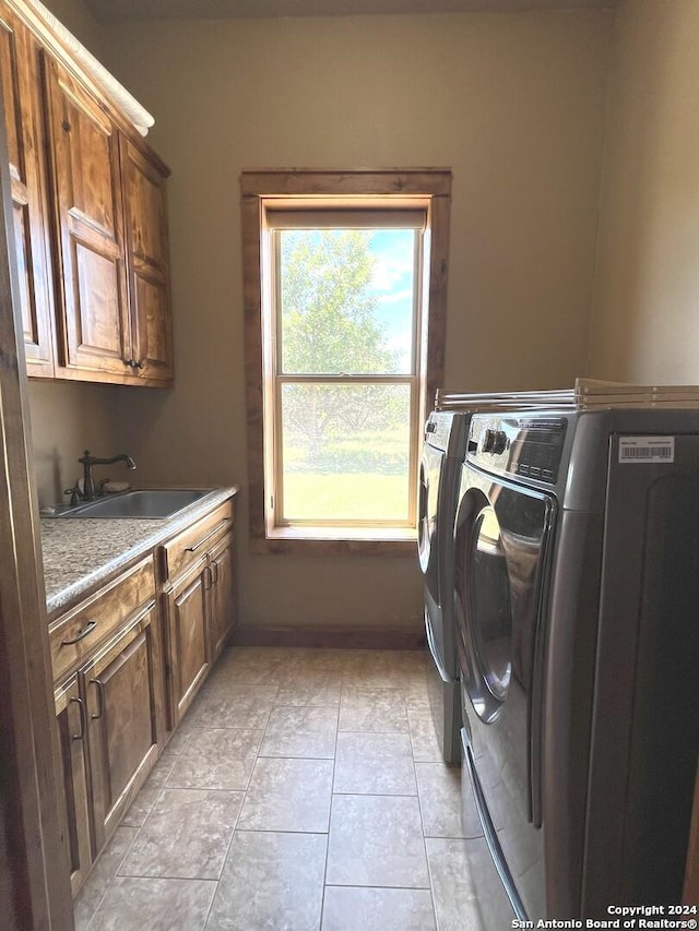 clothes washing area featuring light tile patterned floors, sink, washer and dryer, and cabinets