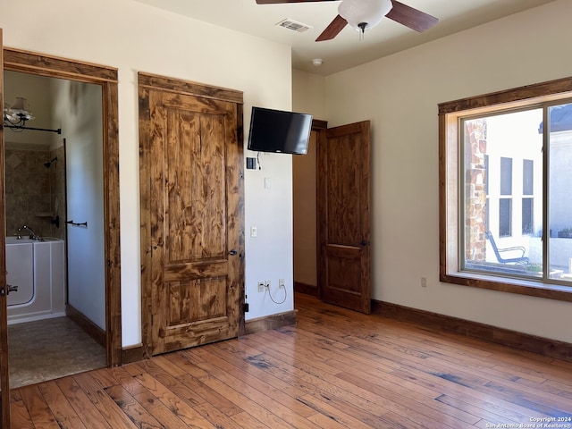 unfurnished bedroom featuring ceiling fan, hardwood / wood-style floors, and multiple closets