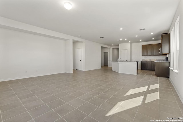 unfurnished living room with light tile patterned floors, baseboards, visible vents, a sink, and recessed lighting