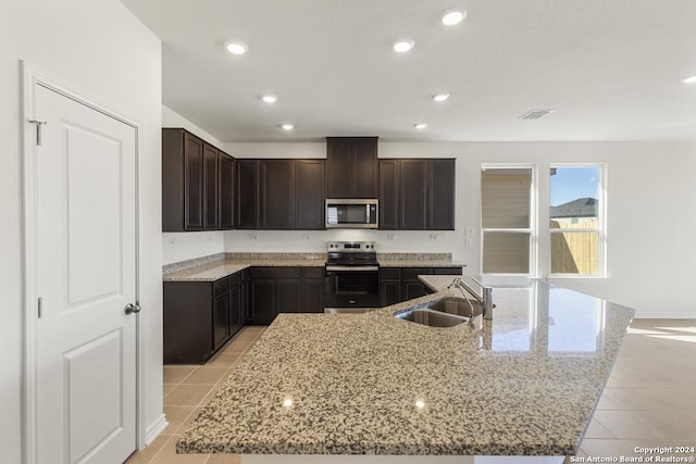 kitchen featuring appliances with stainless steel finishes, light stone counters, a kitchen island with sink, and sink