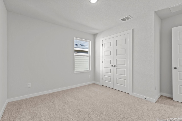 unfurnished bedroom featuring a closet, light colored carpet, and a textured ceiling