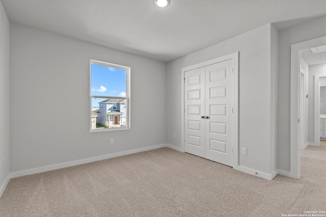 unfurnished bedroom featuring light carpet, a closet, and a textured ceiling