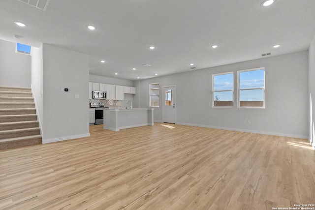 unfurnished living room featuring light wood-style flooring, stairs, baseboards, and recessed lighting