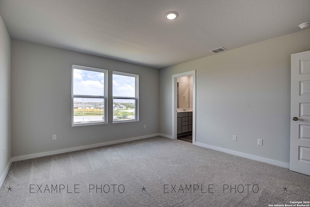 unfurnished bedroom with carpet floors, a textured ceiling, and ensuite bath