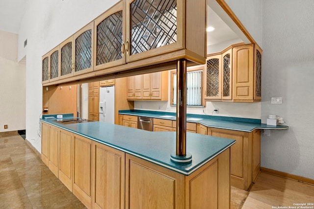 kitchen featuring light brown cabinetry, glass insert cabinets, white fridge with ice dispenser, dishwasher, and baseboards