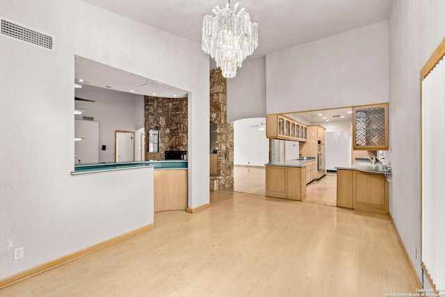 unfurnished living room featuring visible vents, a high ceiling, a chandelier, light wood-type flooring, and baseboards