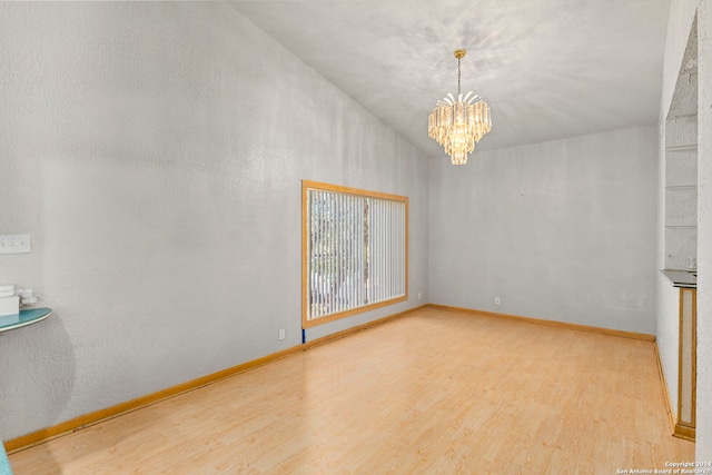 unfurnished room featuring light wood-type flooring, a notable chandelier, and baseboards