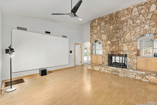 unfurnished living room featuring ceiling fan, arched walkways, a stone fireplace, wood finished floors, and visible vents