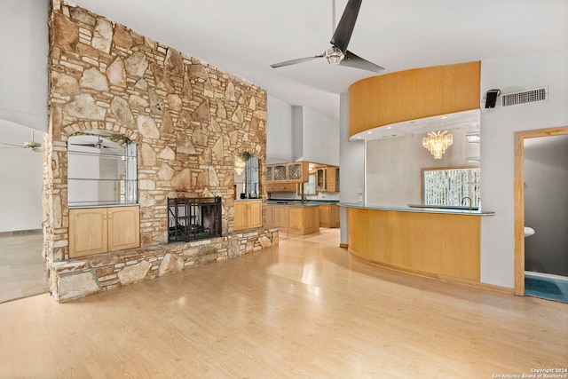 unfurnished living room featuring ceiling fan with notable chandelier, a stone fireplace, light wood finished floors, and visible vents