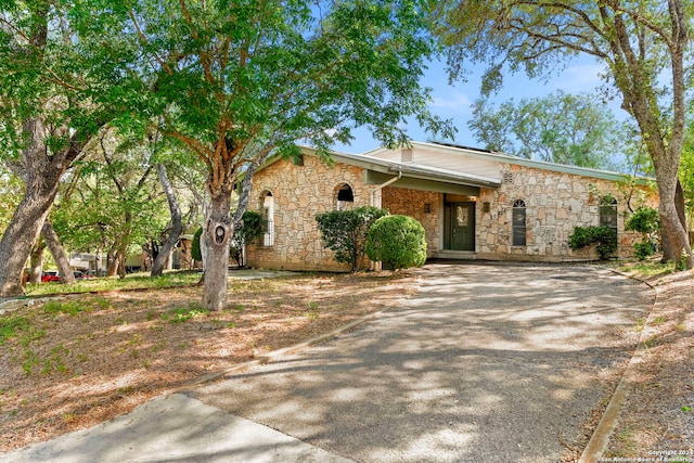 mid-century home with driveway and stone siding