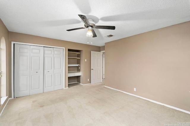 unfurnished bedroom featuring a textured ceiling, ceiling fan, light colored carpet, visible vents, and baseboards