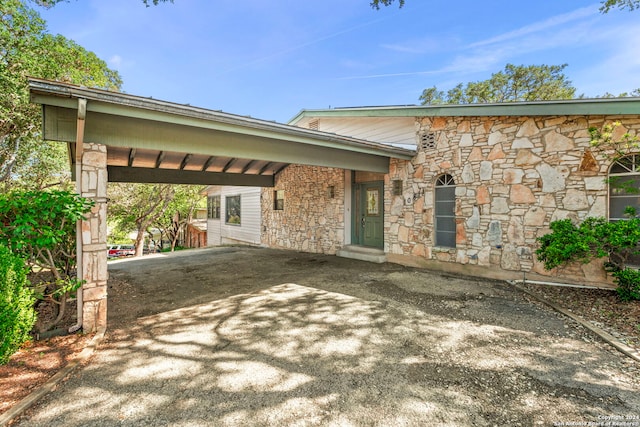 view of front facade with a carport, stone siding, and driveway